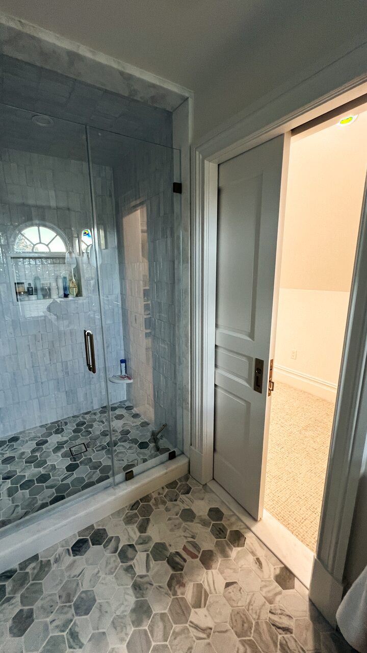 Walk-in shower tiled in marble with a frameless glass enclosure and a hexagon marble floor.