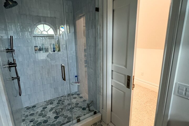 Marble tiled shower with a frameless glass door and hexagon mosaic floor.